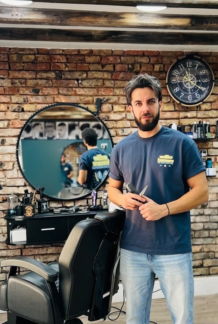 Will, owner of Cygneture Barbers, standing in the shop in Swanland holding scissors and a comb